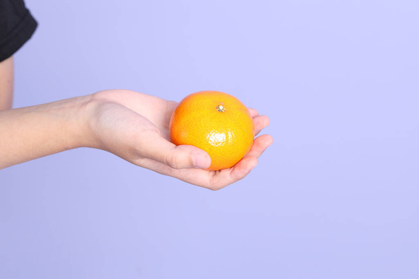 Asijská žena drží pomerančové ovoce na fialovém pozadí. - Fotografie, Obrázek