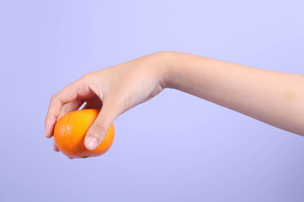 La mujer asiática sosteniendo fruta naranja sobre el fondo púrpura. - Foto, imagen