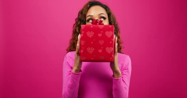 Возбужденная молодая женщина держит подарочную коробку и показывает лицо, розовую ленту, годовщину. Высококачественные 4k кадры - Кадры, видео