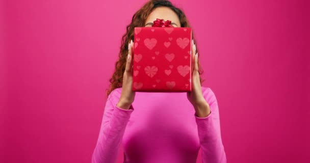Ενθουσιασμένη νεαρή γυναίκα κρατά κουτί δώρου και αποκαλύπτει πρόσωπο, ροζ κορδέλα, επέτειο. Υψηλής ποιότητας 4k πλάνα - Πλάνα, βίντεο