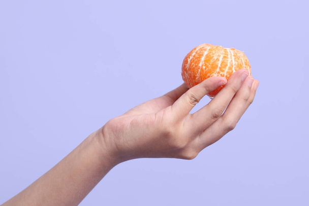 Die Asiatin hält orangefarbene Früchte auf dem violetten Hintergrund. - Foto, Bild