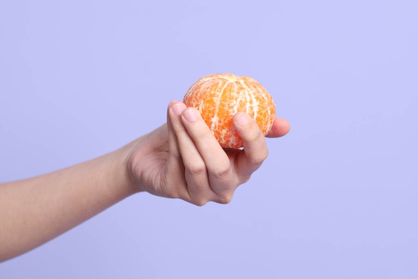 Die Asiatin hält orangefarbene Früchte auf dem violetten Hintergrund. - Foto, Bild