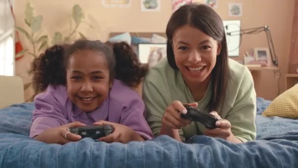 Waist up von fröhlicher afroamerikanischer Mutter und ihrer 10-jährigen Tochter, die zusammen Spaß beim Spielen von Videospielen haben - Filmmaterial, Video