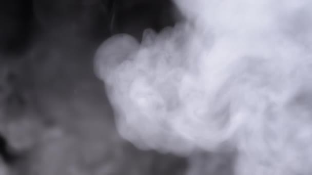 Pluimen van dikke ijzige wolken van rook of stoom vullen de ruimte in wazige beweging. Draaien van zachte witte krullen van wolken rook uit vape, sigaretten oplossen op een zwarte achtergrond. Textuur. Volledig frame. - Video