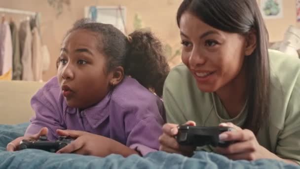 Mellkas fel boldog fiatal Biracial nő és az ő 10 éves lánya pihen az ágyban együtt játszik videojátékok - Felvétel, videó