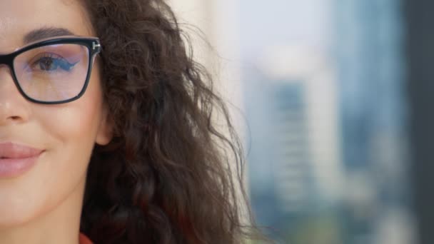 Half face portrait of beautiful mixed race gorgeous woman in fashionable eyeglasses, with curly hair smiling at camera looking confident. Pretty diverse model face, copy background blurred urban city - Footage, Video