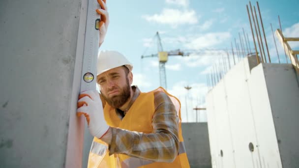Um jovem trabalhador verifica o nível da parede com um nível de espírito. Retrato de trabalhador de construção caucasiano usando construção de verificação de nível - Filmagem, Vídeo