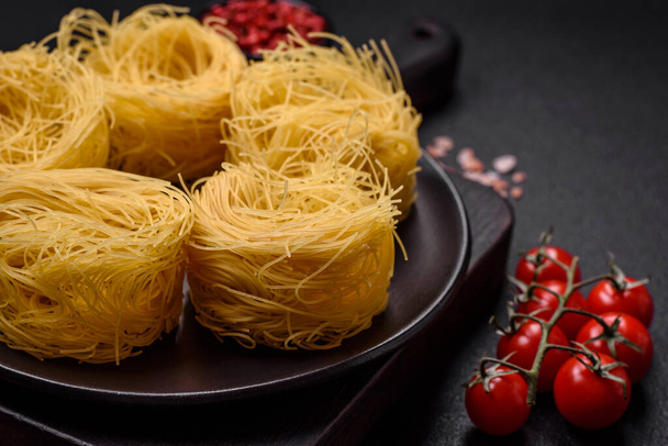Raw capellini pasta or noodles with salt and spices on a dark concrete background - Photo, Image