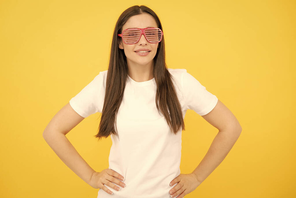 Wesoła dziewczyna w wielkich bif zabawnych okularach przeciwsłonecznych. Portret młodej kobiety w śmiesznych okularach na żółtym tle - Zdjęcie, obraz