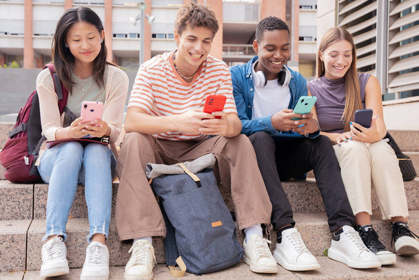  czworo wielorasowych przyjaciół bawiących się korzystając z sieci społecznościowych ze swoim urządzeniem komórkowym - Zdjęcie, obraz