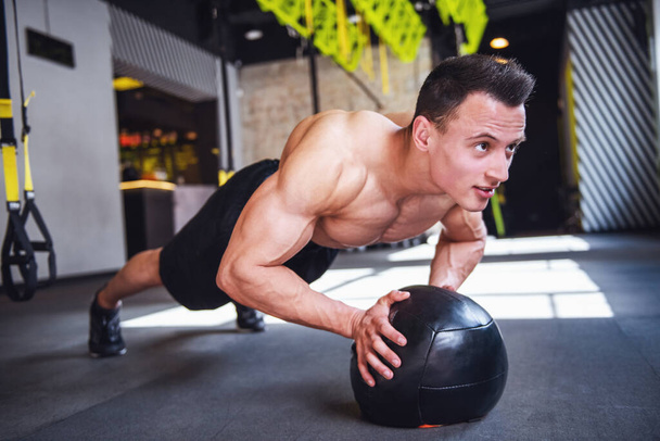 Guapo joven deportista muscular está trabajando con una pelota de medicina en el gimnasio
 - Foto, Imagen