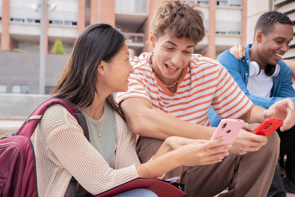  estudantes sorrindo multiétnicos sentados ao ar livre usando um telefone celular para conversar online. Conceito de vida universitária - Foto, Imagem