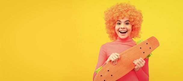 Joyeux fille cool avec des cheveux orange en rose poloneck sourire tenant pennyboard, planche à roulettes. Enfant adolescent drôle sur la fête, en-tête de bannière affiche avec espace de copie - Photo, image