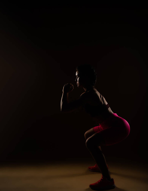 Fit female person doing squats in studio. She is exercising her legs - Photo, Image