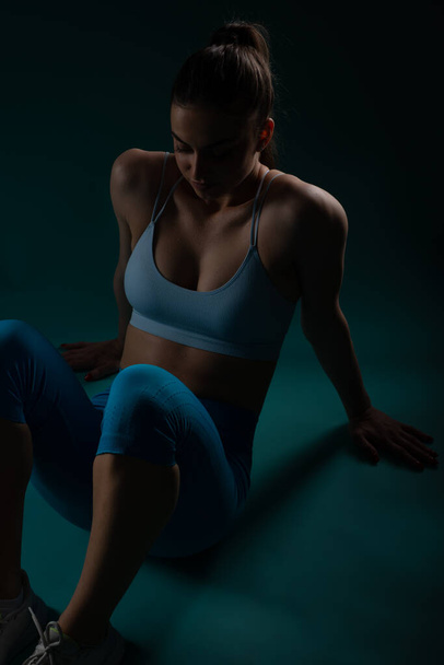 Selbstbewusste, fitte Frau trainiert im dunklen Hintergrundstudio - Foto, Bild