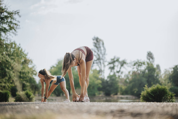 Fit Girls Training Outdoors: Inspirerende sportieve vrouwen die zich uitstrekken en opwarmen in een groen park voor pre-workout fitness - Foto, afbeelding