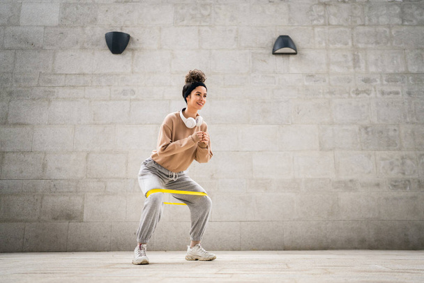 Une femme adulte caucasienne athlète entraînement féminin avec élastique élastique bandes de résistance en plein air dans la ville sur fond de béton étirement dans heureux brune santé et fitness concept copier l'espace - Photo, image