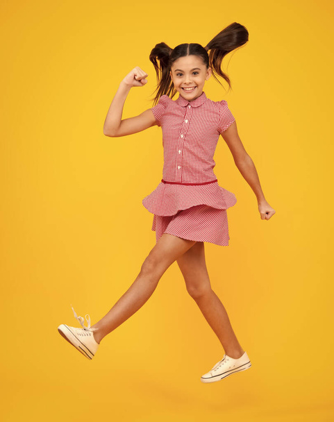 Onnellinen teini, positiivinen ja hymyilevä tunteita teini tyttö. Täysikokoinen kuva positiivinen teini tyttö hypätä liikkeen kesän mekko, muoti lapset asu eristetty yli keltainen tausta - Valokuva, kuva