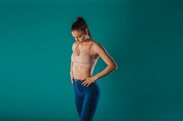 Confident fit girl poses in a studio, showcasing her muscular physique and fitness motivation. With a turquoise background, this young woman inspires with her powerful presence and impressive results. - Photo, Image