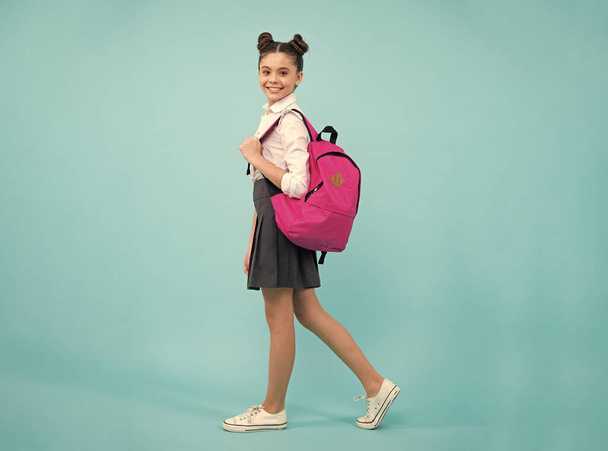 Školačka ve školní uniformě se školní taškou. Dospívající dívka studentka na modrém izolovaném pozadí. Výuka znalostí a vzdělávání dětí koncepce. Šťastná školačka - Fotografie, Obrázek