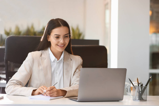 Happy woman using modern laptop at white desk in office - Photo, Image