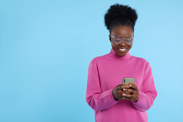 Happy young woman with smartphone on light blue background. Space for text - Φωτογραφία, εικόνα