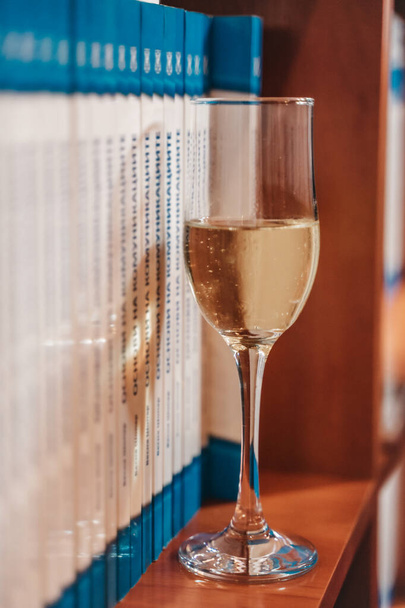 Ein Glas Champagner im Bücherregal. Nahaufnahme. - Foto, Bild