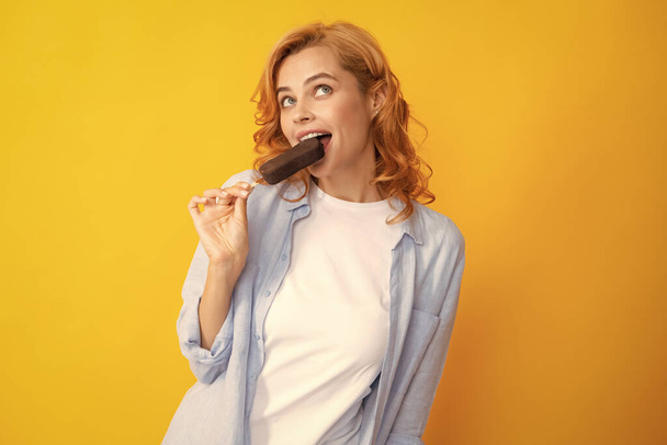 Молода жінка їсть морозива з шоколадною глазур'ю на жовтому тлі. Смішна руда жінка з морозивом
 - Фото, зображення