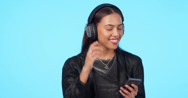 Woman, listening to music with smartphone and headphones, dancing to playlist and fun on blue background. Young female person, audio streaming and radio, social media and gen z with mockup space. - Footage, Video