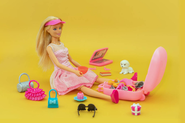 2023年10月9日。 ロシアのバルナウル:バービーはピンクの背景にピンクのドレスを着た旅行者の人形です. 人形がスーツケースを詰めている. 人形で遊ぶためのさまざまな付属品. - 写真・画像