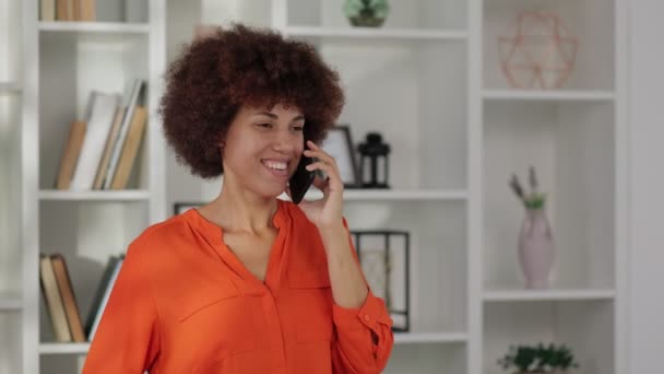 Retrato de mujer afroamericana con el pelo rizado hablando en smartphone y sonriendo en la oficina  - Metraje, vídeo