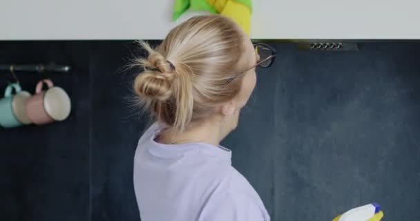 Blondine vrouw reinigt keukenplanken met water spray en doek. jong huisvrouw in bril met moe uitdrukking presteert huis klusjes - Video