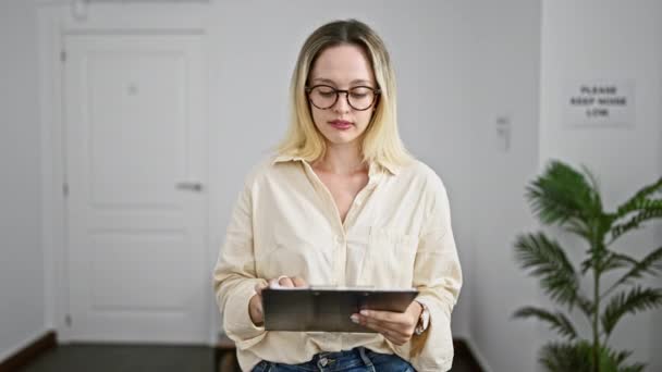 Joven mujer rubia trabajadora de negocios sujetando portapapeles mirando a la oficina - Metraje, vídeo