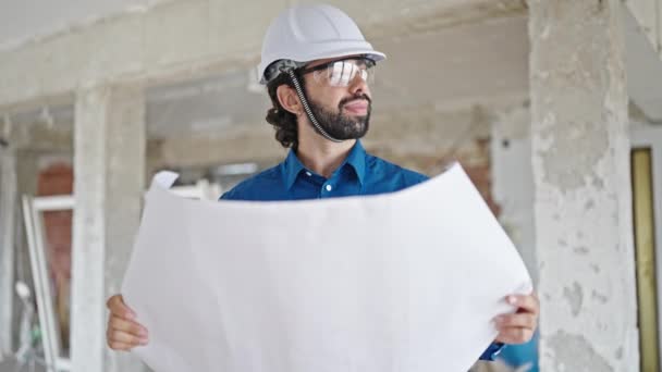 Fiatal spanyol férfi építész kezében tervrajzokkal körülnéz az építkezésen. - Felvétel, videó