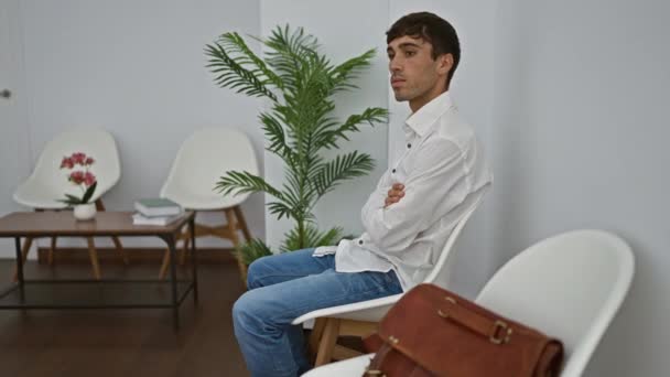 Poważny młody Latynos, elegancki profesjonalista, siedzący w poczekalni, rzucający skoncentrowane spojrzenia w przestrzeń wewnętrzną, niosący sukces. - Materiał filmowy, wideo