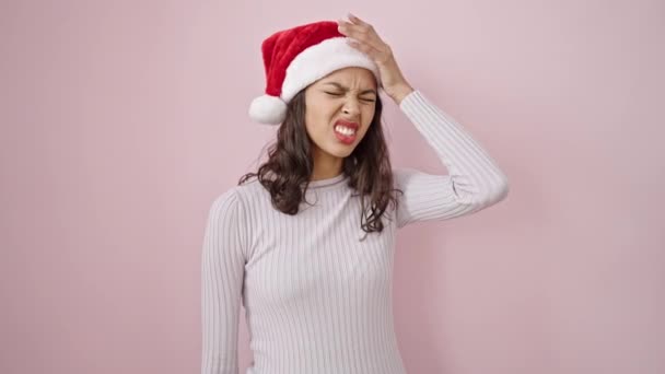 jong mooi latino vrouw het dragen van kerst hoed met hoofdpijn over geïsoleerde roze achtergrond - Video