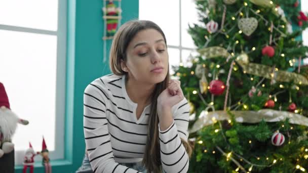Junge schöne hispanische Frau feiert Weihnachten sitzend mit ernstem Gesichtsausdruck zu Hause - Filmmaterial, Video
