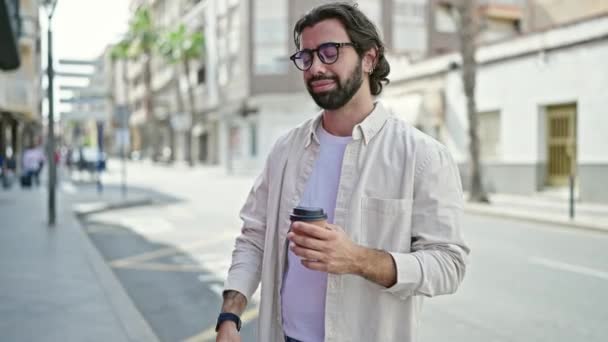 Młody Hiszpan pijący zabiera kawę patrząc na zegarek odchodzący na ulicę - Materiał filmowy, wideo