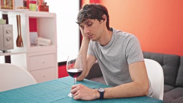 若いヒスパニックの男は,ダイニングルームで考えているテーブルに座ってワインのグラスを保持しています - 映像、動画