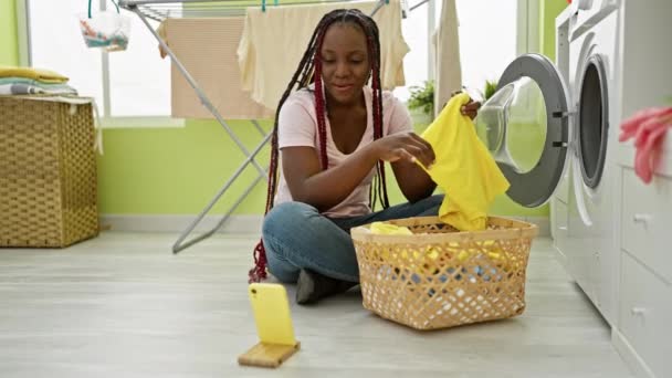 Чарівна афроамериканська жінка радісно телефонує, керуючи домашньою роботою, миючи одяг у пральні свого дому - Кадри, відео