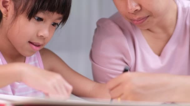 Moeder en dochter tekenen samen met krijtjes. Volwassen vrouw helpt meisje studeren of samen te trekken thuis in de woonkamer. Gelukkige familie. - Video