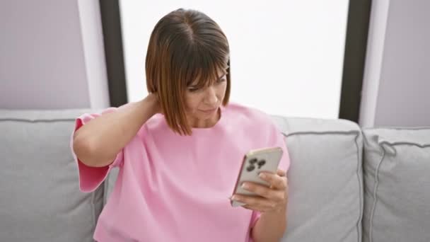 Στρεσαρισμένη νεαρή ισπανίδα γυναίκα που υποφέρει από πόνο στον αυχένα ενώ στέλνει μηνύματα στο smartphone της στο σπίτι - Πλάνα, βίντεο
