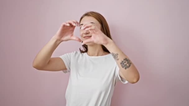 Fiatal nő mosolygós magabiztos csinál szív gesztus kezek felett elszigetelt rózsaszín háttér - Felvétel, videó