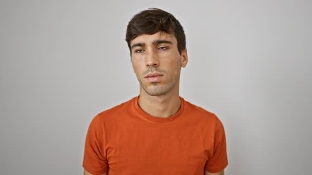 Jonge, knappe Spaanse man voelt het geluid te luid, bedekt serieus oren met handen staande door een geïsoleerde witte achtergrond, kijkend weg in concentratie - Video