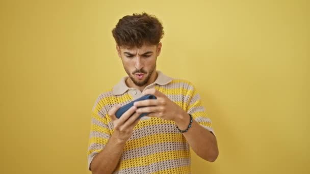Zelfverzekerde jonge Arabier man vreugdevol vieren zijn gaming win, glimlachen tijdens het spelen van videospel op zijn smartphone tegen geïsoleerde gele achtergrond - Video