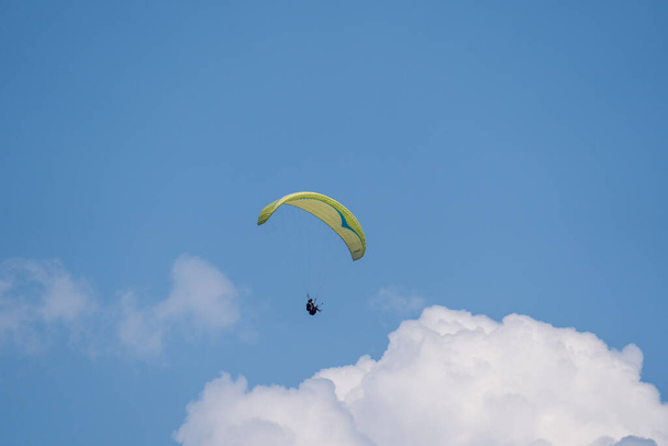 Parlak mavi gökyüzünde kabaran bulutlarla yamaç paraşütü yapan biri.. - Fotoğraf, Görsel
