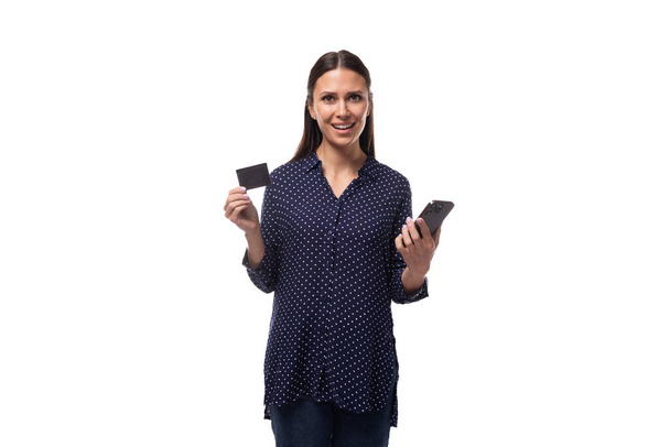 青いシャツとジーンズを着た若い成功したブルネットの女性は,クレジットカードとスマートフォンを保持しています. - 写真・画像