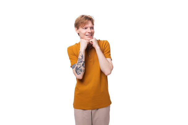 junger rothaariger kaukasischer Student mit Tätowierung in einem Senf-T-Shirt auf weißem Hintergrund. - Foto, Bild