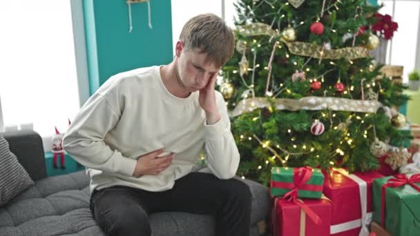 Νεαρός καυκάσιος άνδρας που υποφέρει από στομαχόπονο γιορτάζει τα Χριστούγεννα στο σπίτι - Πλάνα, βίντεο