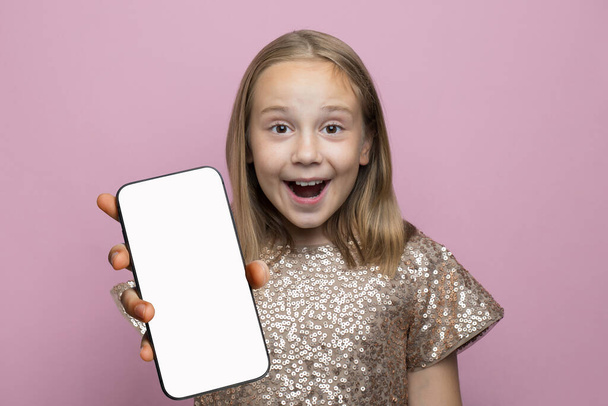 Dość zszokowany radosny dziewczynka trzyma smartfon z pustym białym ekranem wyświetlacz dla nowej aplikacji lub mobilnej stronie internetowej na różowym tle - Zdjęcie, obraz